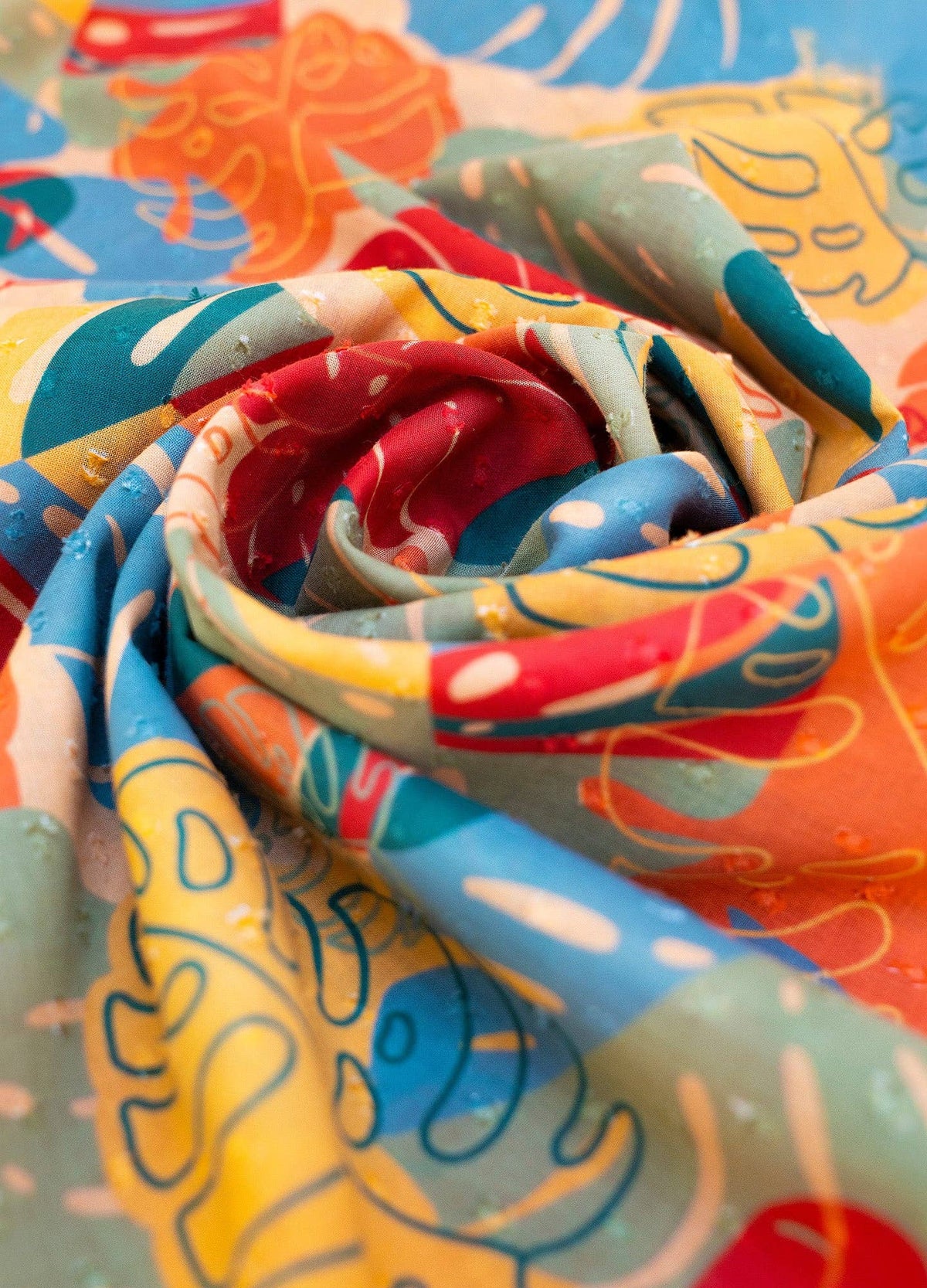 Close up of colorful fabric of scarf with abstract patterns and tropical leaf outlines in red, blue, yellow, and orange.