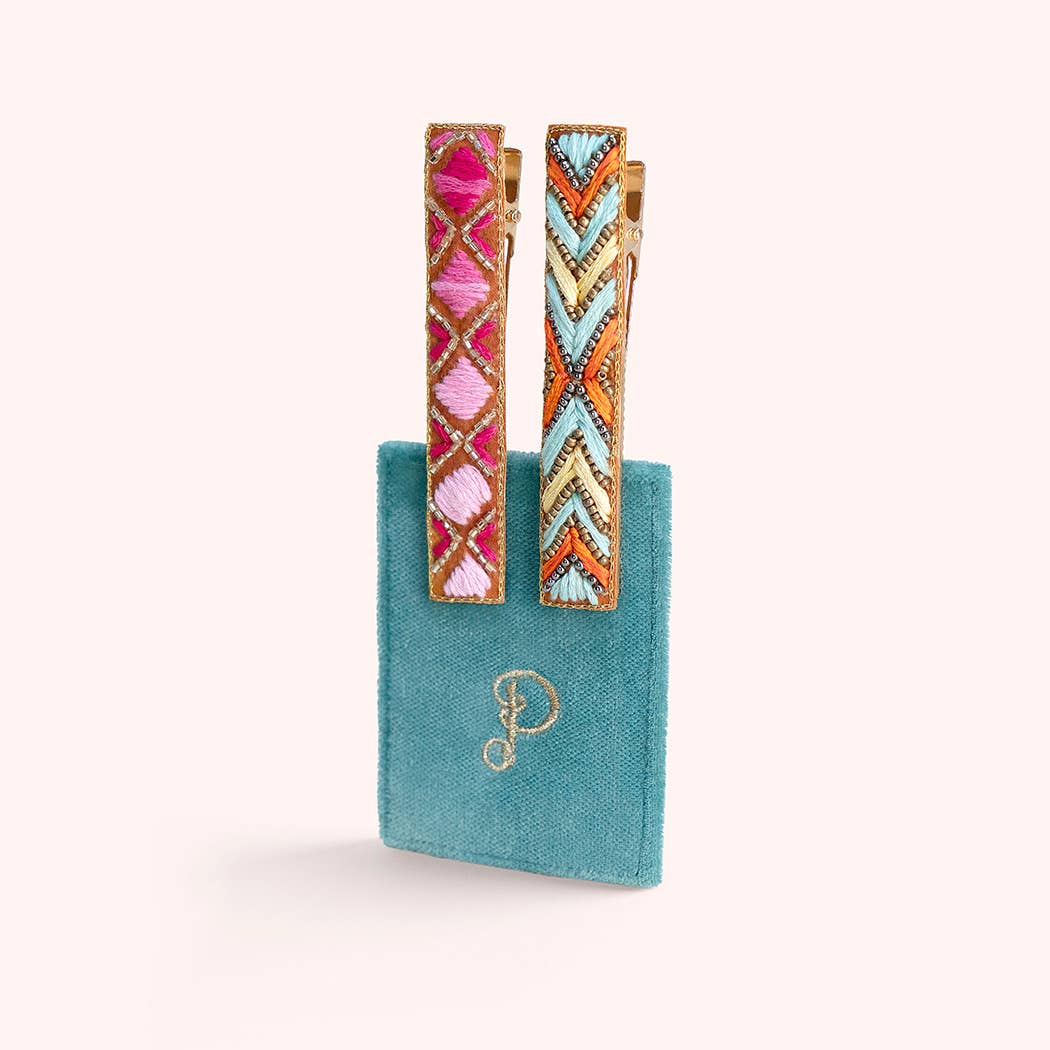 Colorful geometric hair clips on a turquoise card with a gold letter 'P' on a white background