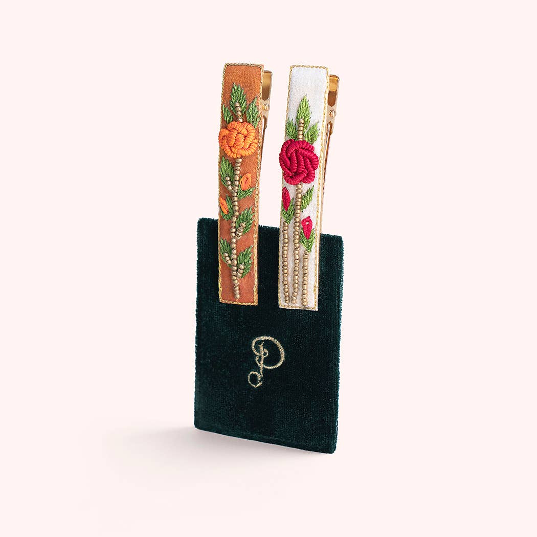 Two embroidered hair clips featuring a floral design on a green card on a white background