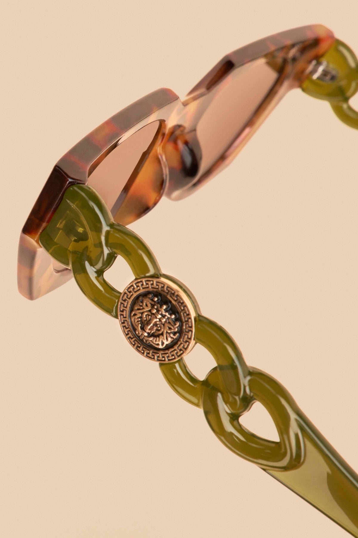 Detailed view of temple arm of olive tortoiseshell sunglasses on a beige background