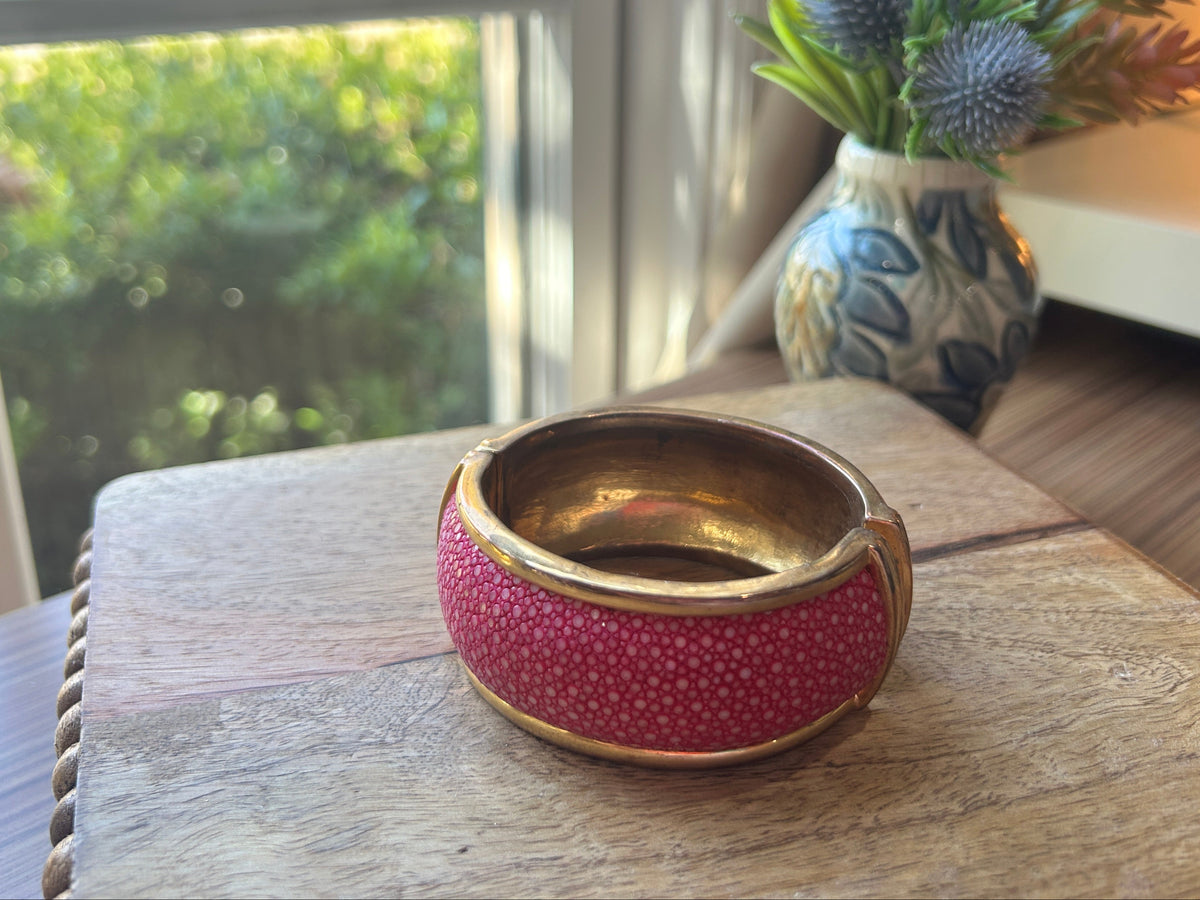Pink and brass toned bracelet on a wood surface. Flowers in background