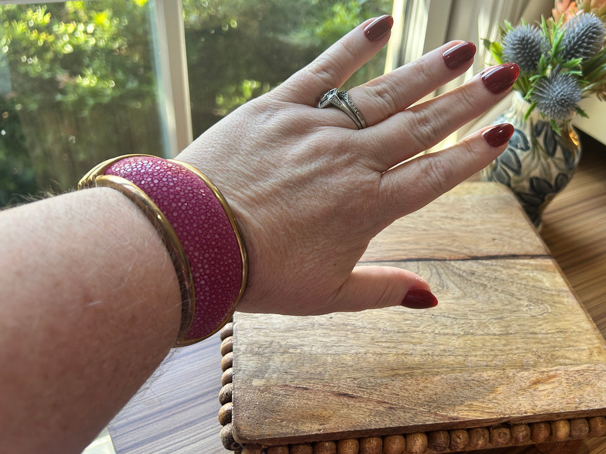 A pink and brass toned bracelet on a woman's arm, flowers in background