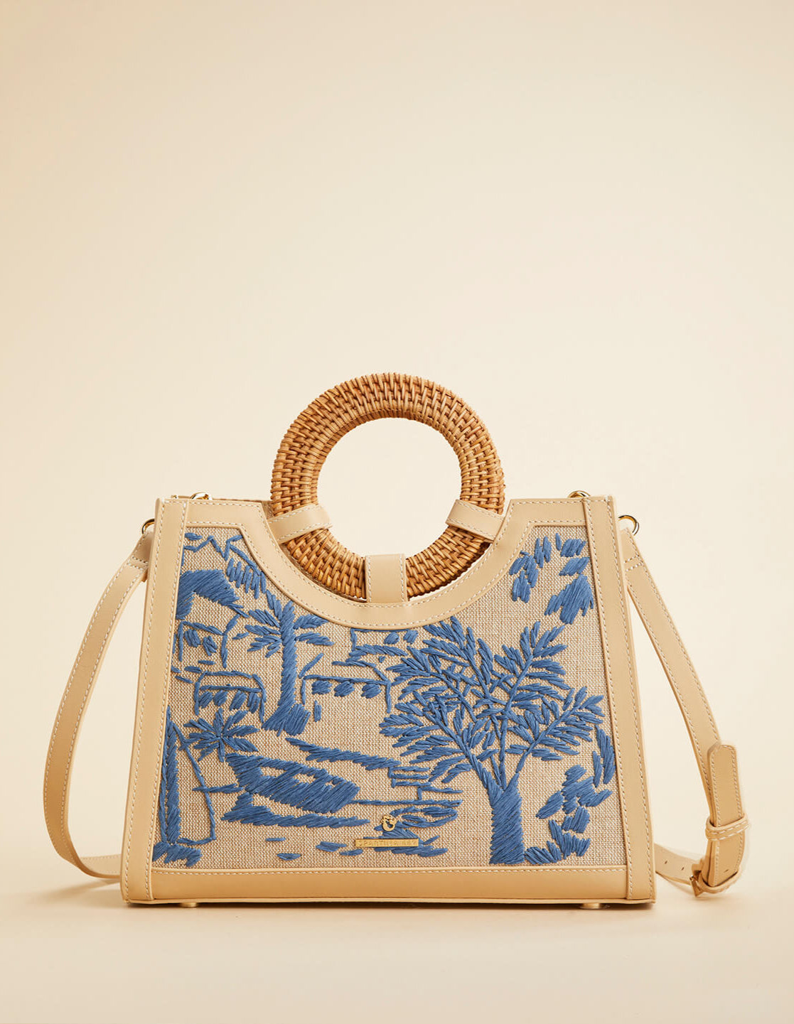 Beige handbag with blue embroidered design and woven handle on a beige background