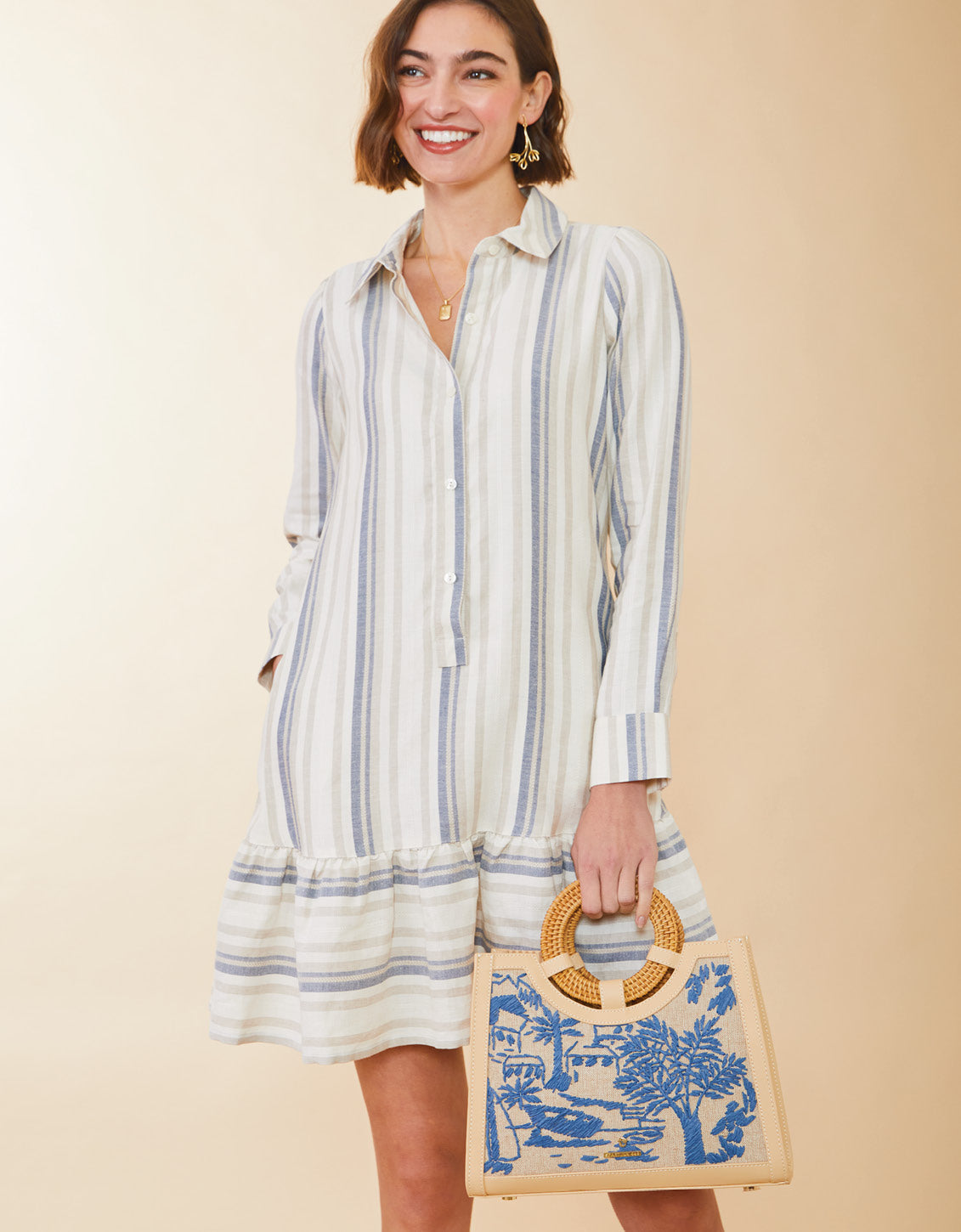 Woman wearing a striped dress holding a blue and white patterned bag against a beige background