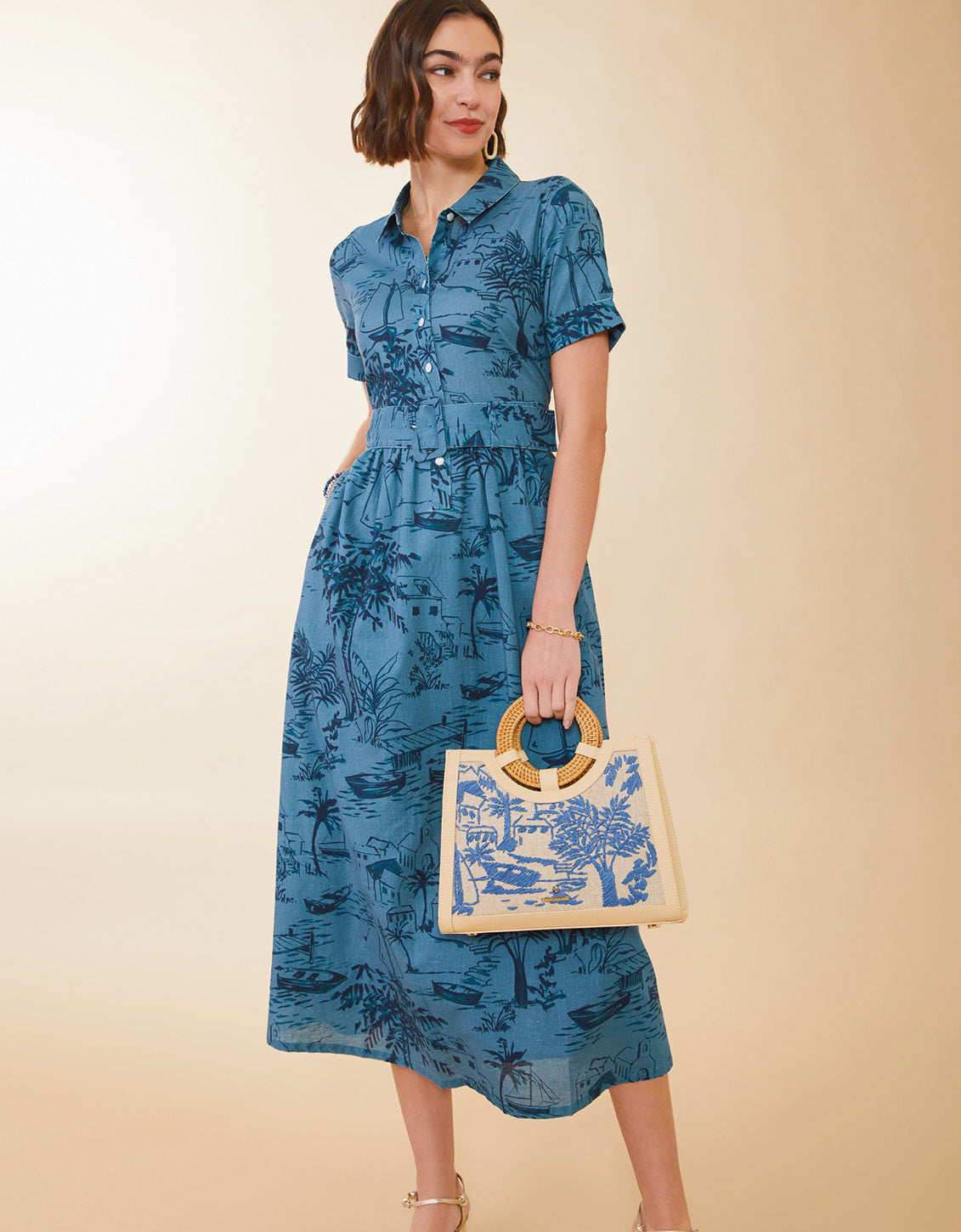 Woman wearing a blue floral dress holding a matching handbag against a beige background