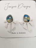 Pair of earrings with white geometric shapes and blue and gold center on a branded card.