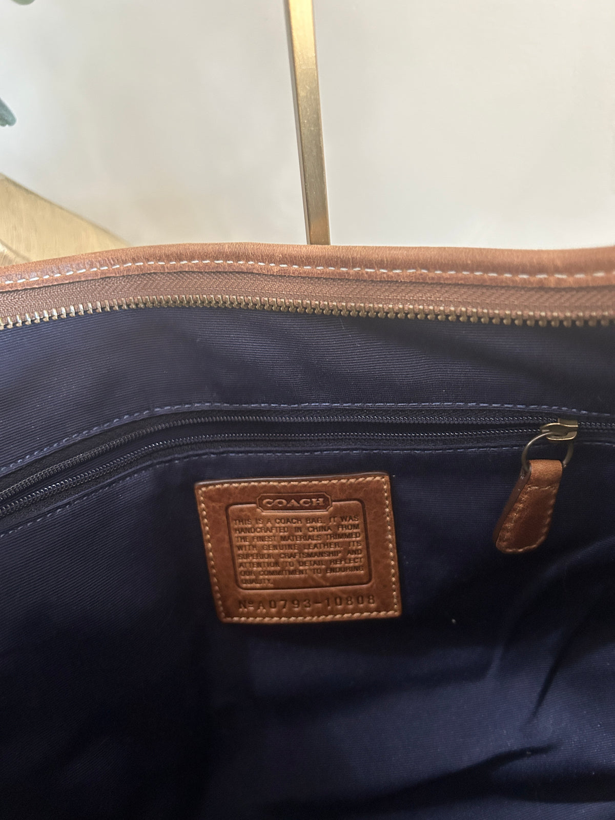 Interior photo of a brown leather trim bag with a blue liner and a Coach branded brown leather creed tag verifying authenticity