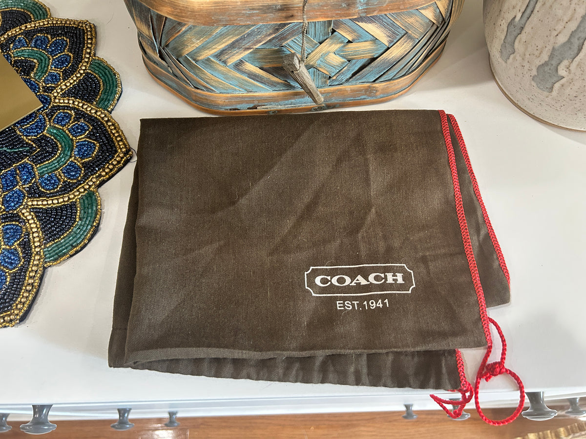 Brown Coach branded dust bag folded on a white shelf with home decor. 
