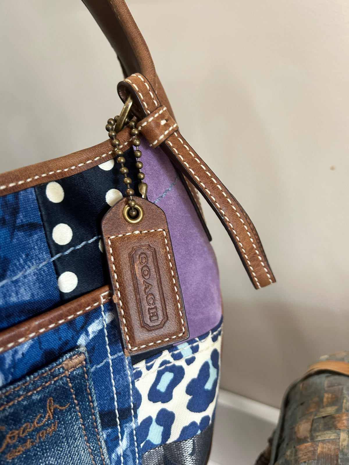 Close up of the Coach branded hangtag on a blue, brown, and purple patchwork bag.
