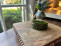 A green and brass bracelet on a wooden surface, flowers in background