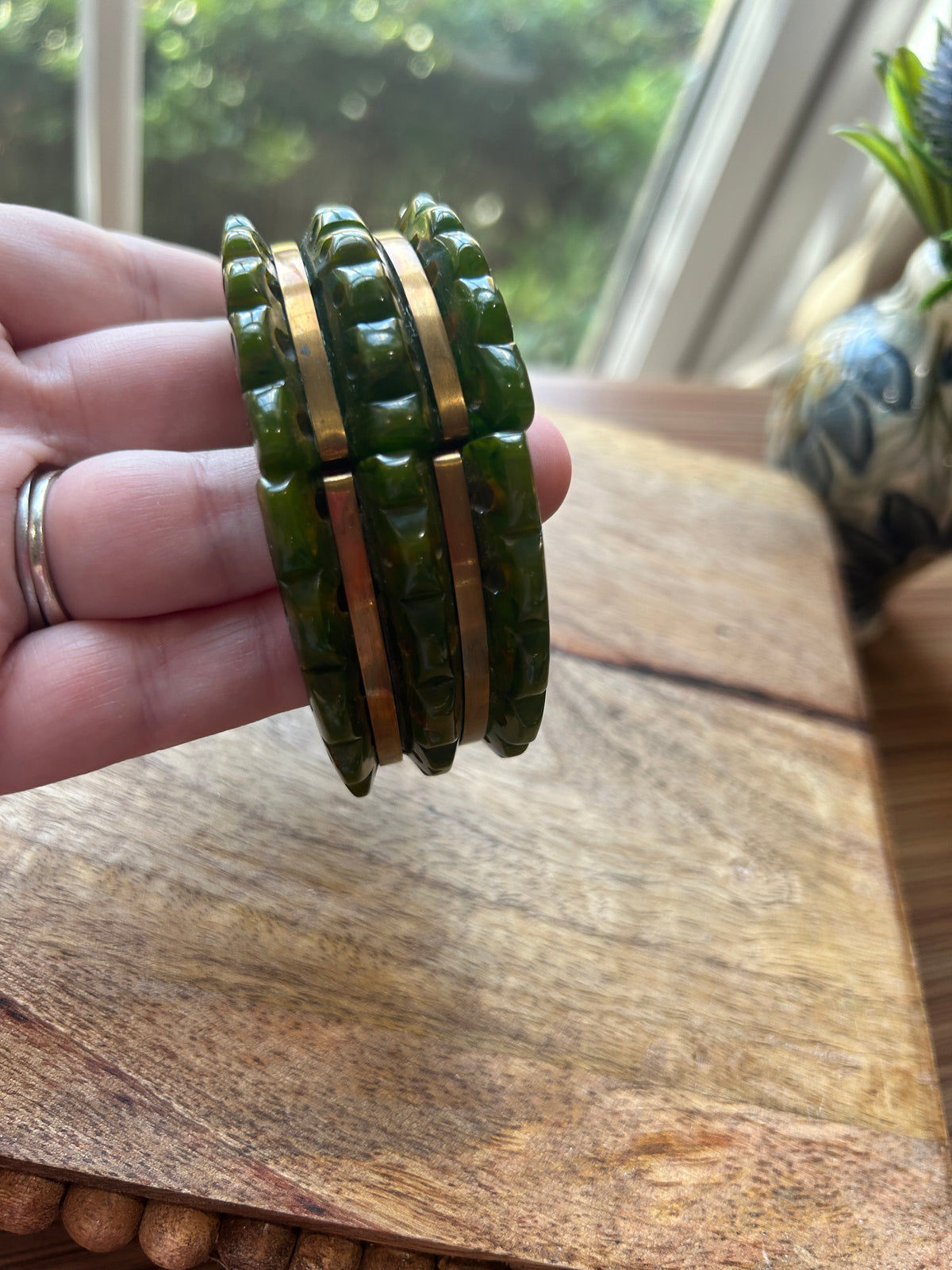 A green and brass toned bracelet held in a hand