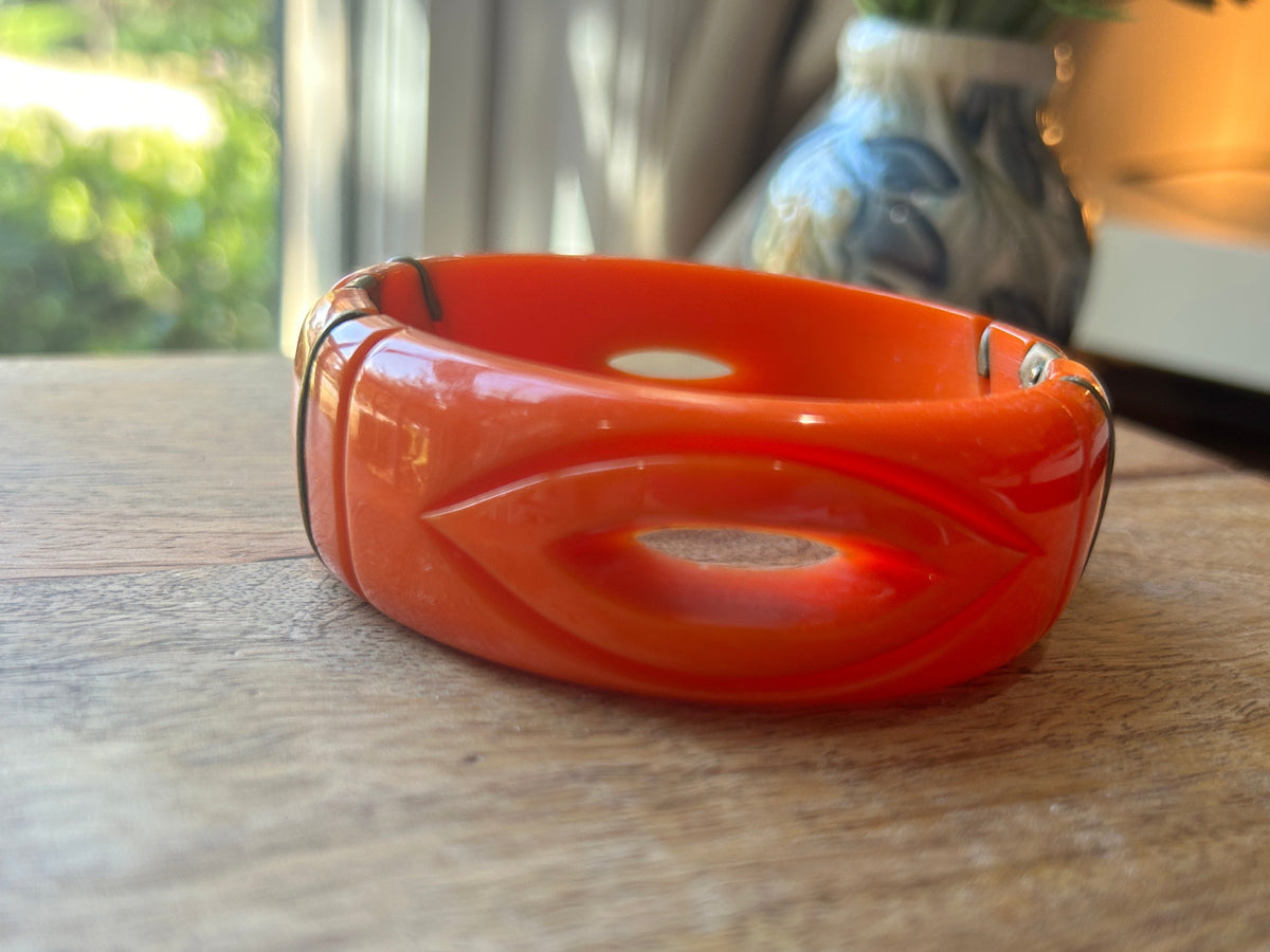 An orange bangle bracelet with carved eye shape on a wood surface