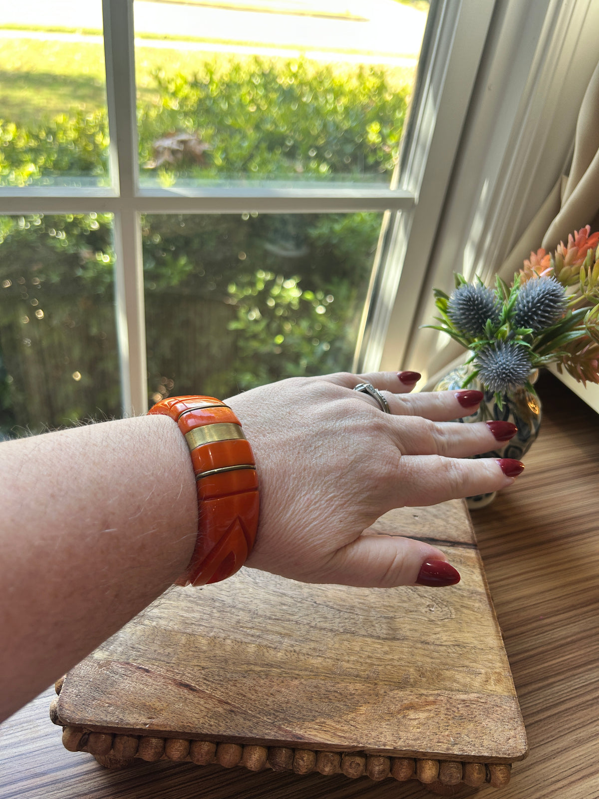 An orange bangle on a woman's arm, brass colored metal bands