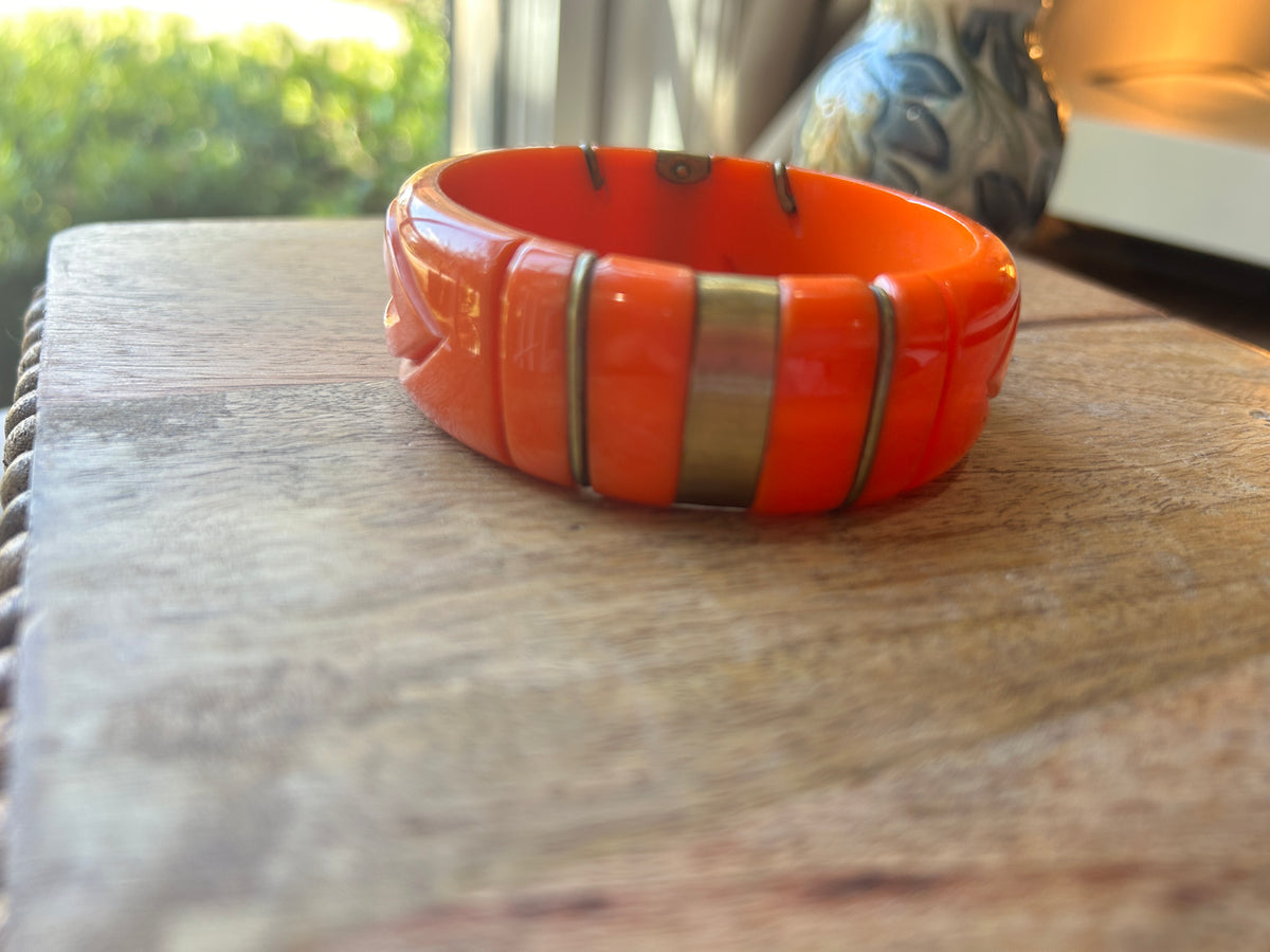 an orange bangle with bands of metal on a wood surface