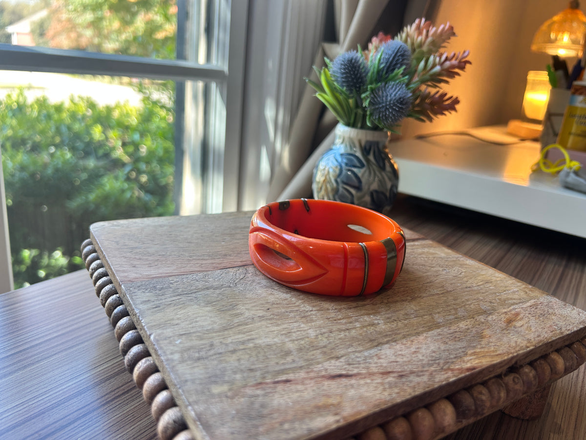 An orange bangle bracelet on a wood surface with flowers in the background