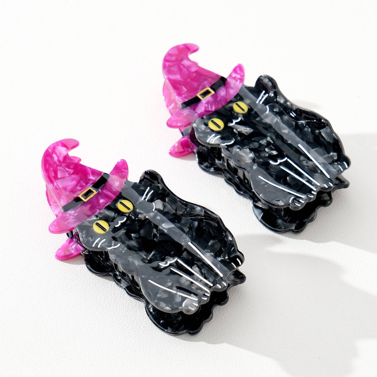 Two black cat-shaped hair clips with purple witch hats on a white background