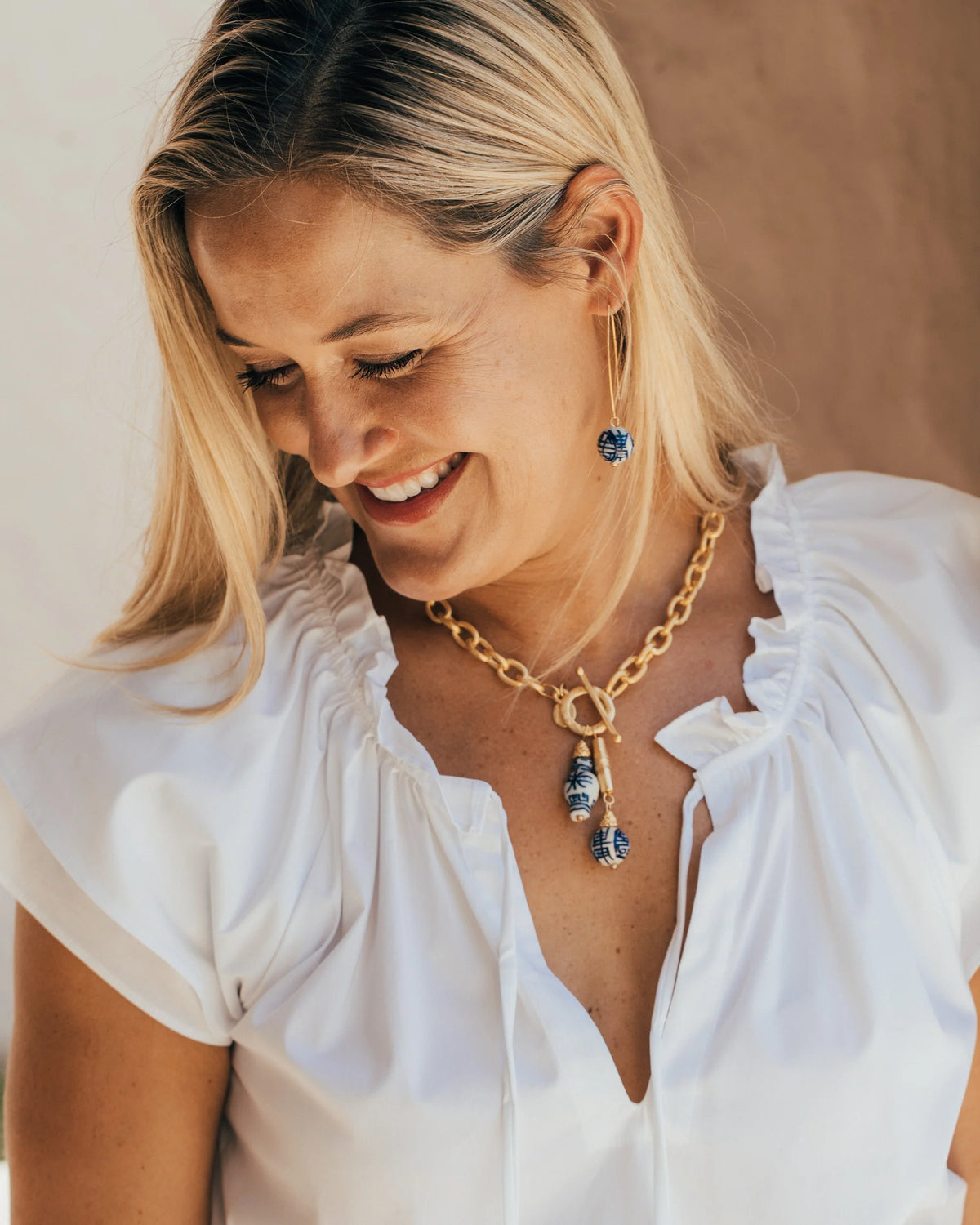 Woman wearing a gold necklace with blue pendant and matching earrings against a neutral background