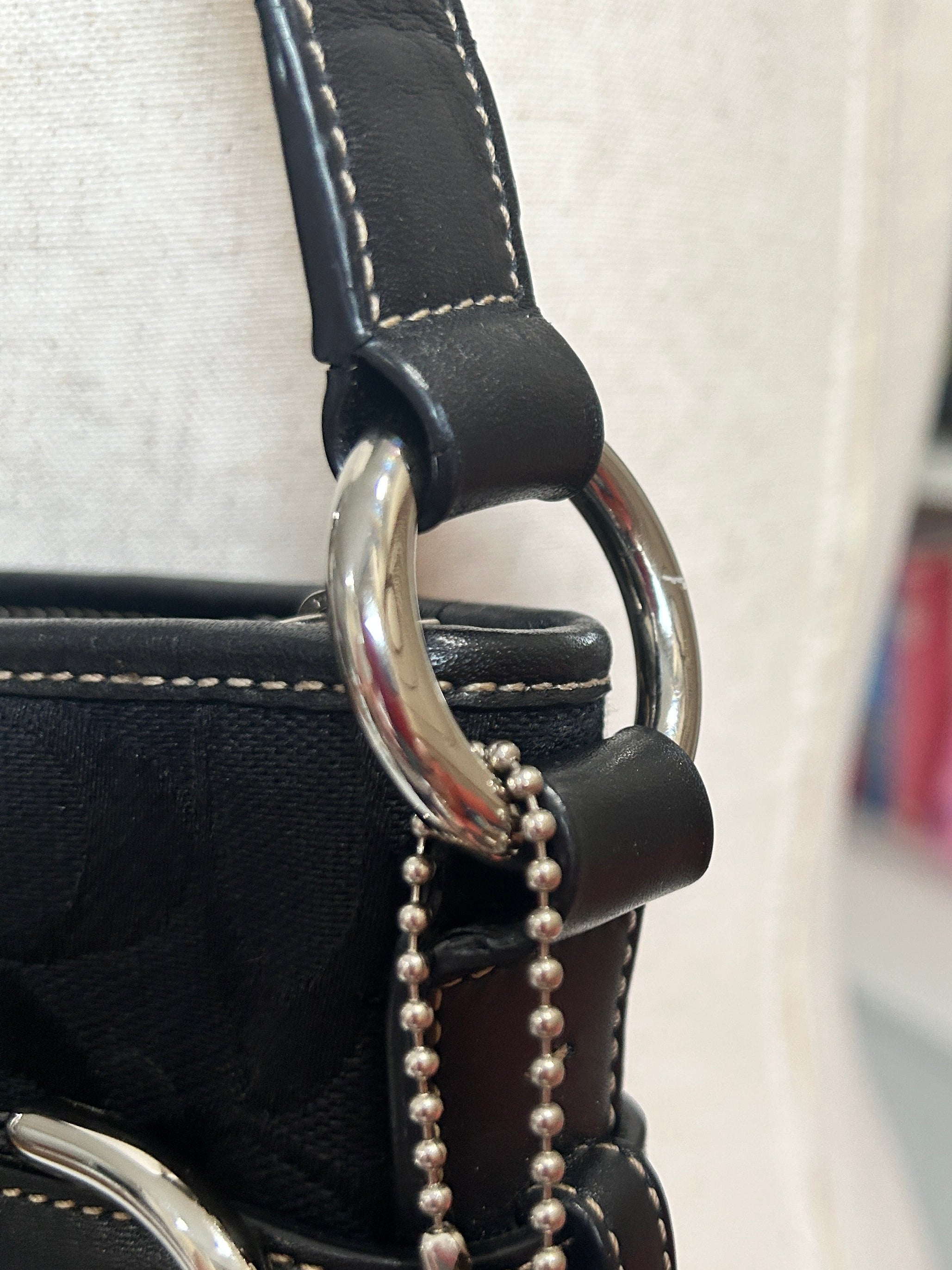 Close-up of a black leather coach handbag with a silver chain and clasp, blurred background.