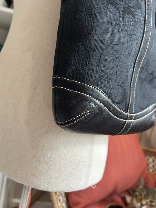 Close-up of a black textured bag with white stitching on a beige surface.