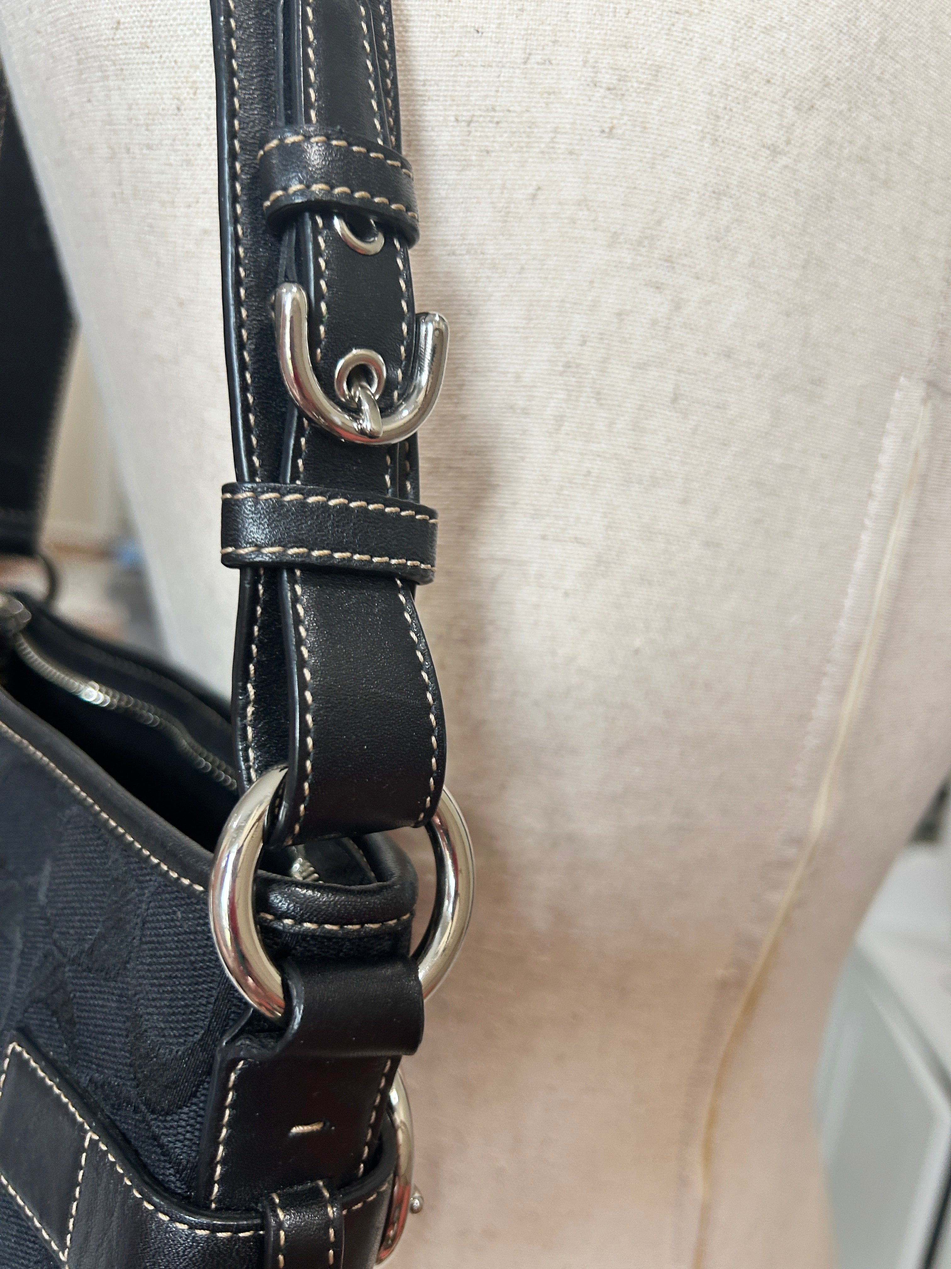 Close-up of a black coach signature bag with metal rings on a beige background